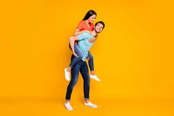 Foto de corpo inteiro de duas pessoas engraçadas cara carregando senhora piggyback conhecer aventuras de verão juntos usar casual moda azul laranja camisetas jeans isolado cor amarela fundo — Fotografia de Stock