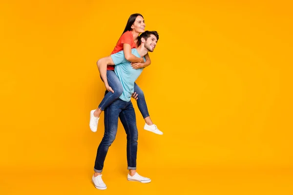 Full length photo of two funny people guy carrying lady piggyback meet summer adventures together wear casual trendy blue orange t-shirts jeans isolated yellow color background — 스톡 사진