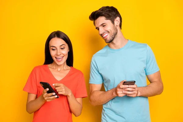 Foto de dos divertido chico señora personas pareja mantenga los teléfonos mostrando dedo comentarios positivos reposts excitados desgaste casual azul naranja camisetas aisladas color amarillo fondo —  Fotos de Stock