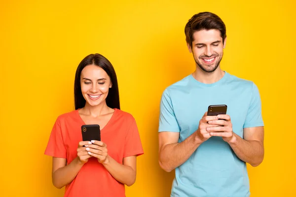 Photo de deux drôles de gars dame gens couple tenir téléphones bras intéressé lecture réseau social article porter casual bleu orange t-shirts isolé couleur jaune fond — Photo