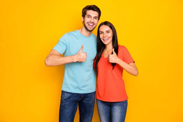 Foto de divertido dos personas pareja en el amor chico dama abrazo levantando dedos pulgar expresando acuerdo desgaste casual azul naranja camisetas jeans aislados sobre fondo de color amarillo —  Fotos de Stock