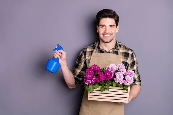 Portret van positieve vrolijke man bloemist werknemer met een eigen kleine tuin zorg over planten bloemen spray sproeier dragen geruite ruitjes shirt geïsoleerd over grijze kleur achtergrond — Stockfoto