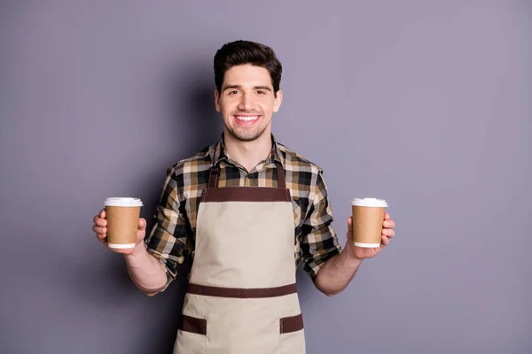Photo of attractive worker guy holding hands two paper coffee cups inviting visitors try aroma coffee professional barista wear apron plaid shirt isolated grey color background — 스톡 사진