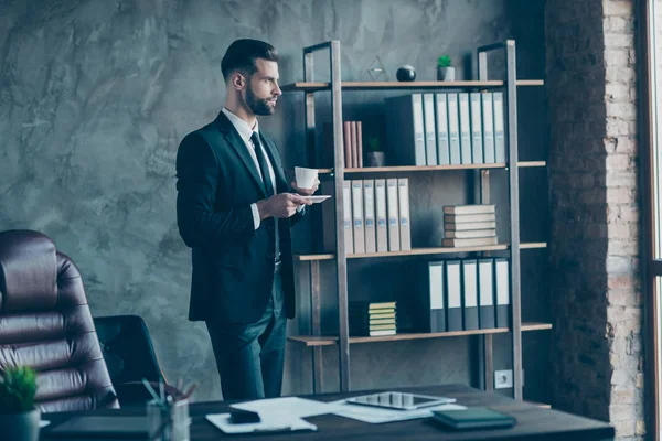 Foto de perfil de un hombre de negocios exitoso persona segura de sí misma sosteniendo taza de café buscando ventana usar camisa de chaqueta negra traje de corbata oficina de pie en el interior — Foto de Stock