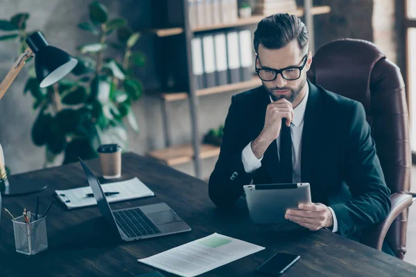 Photo of attentive handsome business guy focused on reading e-reader report checking finance income numbers sums wear specs black blazer shirt tie suit sitting chair office indoors — Stock Photo, Image