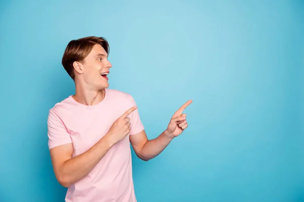 Foto von attraktiven aufgeregten Kerl zeigt Finger leeren Raum Beratung neue Einkaufspreise süchtigen Käufer tragen lässige rosa T-Shirt isoliert blaue Farbe Hintergrund — Stockfoto