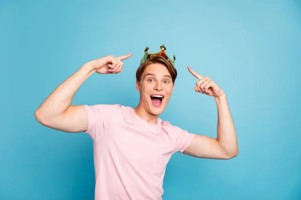 Foto di bello giovane ragazzo divertente umore studenti partito indicando dita oro tiara sulla testa famosa persona celebrità stato indossare casual rosa t-shirt isolato blu colore sfondo — Foto Stock