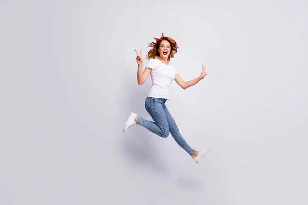 Повнометражний вигляд на її тіло вона приваблива весела весела дівчина стрибає в повсякденному одязі, весело показуючи v-знак ізольовано на світлому білому пастельному фоні — стокове фото