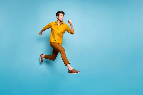 Full längd profil foto av rolig upphetsad kille hoppar hög hastighet nästan få mållinjen bära gul skjorta byxor isolerad blå färg bakgrund — Stockfoto
