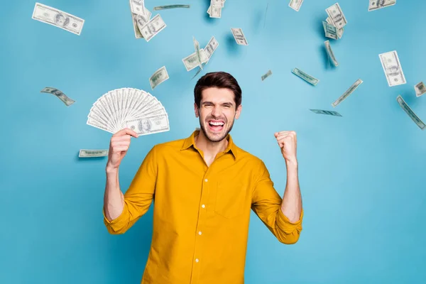 Photo of excited ecstatic cheerful emotional man expressing overjoying feelings with face holding bucks with hand standing in cash rain isolated over blue pastel color background — 스톡 사진