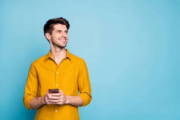 Photo de toothy beau huy portant chemise jaune tenant le téléphone avec les mains souriantes rayonnant à l'espace vide à proximité isolé sur fond bleu pastel — Photo