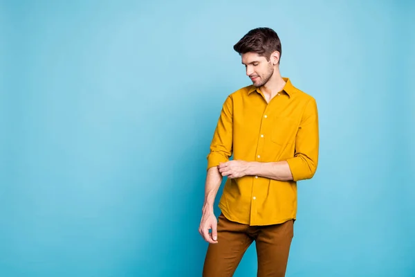 Photo of masculine intelligent man touching his sleeve of yellow shirt standing confidently near empty space isolated over pastel blue color background — 스톡 사진