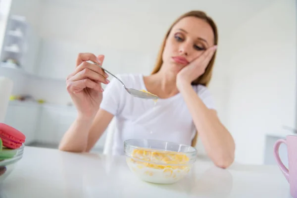 Photo of beautiful blond upset housewife holding spoon dont want eat milk breakfast cornflakes tired of dieting bored sitting table white light kitchen indoors — 스톡 사진