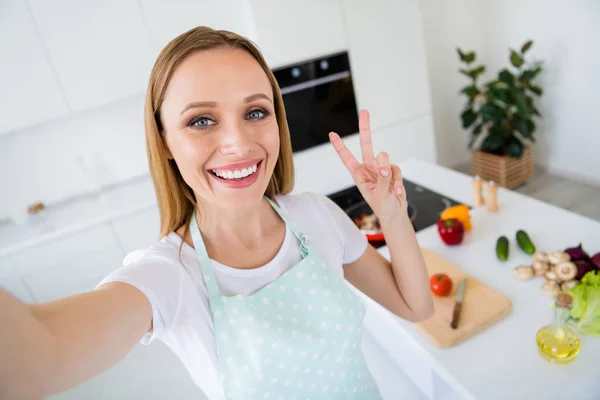 Foto van mooie huisvrouw weekend ochtend koken tonen v-teken maken selfies presenteren volgelingen traditionele familie recept maaltijd witte keuken binnen — Stockfoto