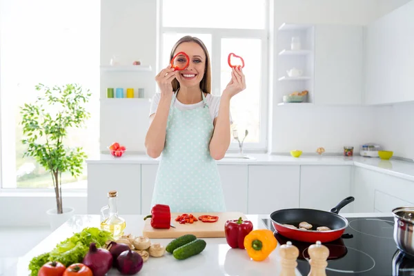 Foto de dona de casa encantadora desfrutar de fim de semana manhã cozinhar saboroso jantar segurando fatia de pimenta vermelha perto do olho infantil despreocupado humor stand cozinha luz branca dentro de casa — Fotografia de Stock