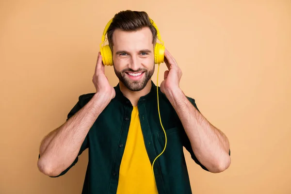 Foto von netten gutaussehenden Hipster Kerl hält Hände cool modernen gelben Kopfhörer hören populäre Songs gute Laune tragen lässiges Outfit isoliert beige Farbhintergrund — Stockfoto