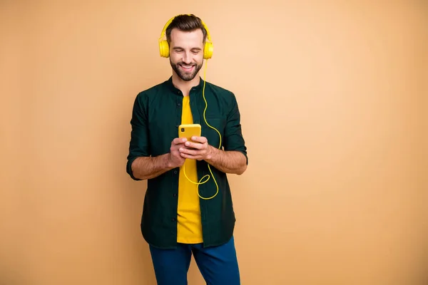 Foto von attraktiven lustigen Kerl hält Telefon Hände hören Jugendlieder cool modernen gelben Kopfhörer tragen lässige Kleidung isoliert beige Farbhintergrund — Stockfoto