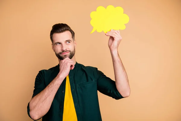 Photo of attractive nice guy holding hand paper cloud thinking over dialogue answer creative person arm on chin tricky sly mood wear casual hipster clothes isolated beige color background