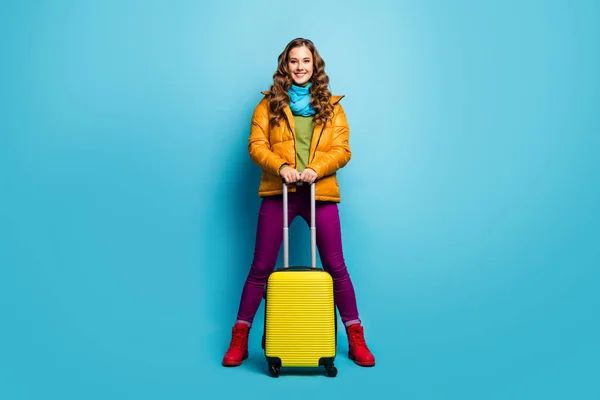 Volledige lengte foto van mooie dame reiziger in het buitenland houden rollende tas koffer luchthaven registratie vlucht dragen gele overjas blauwe sjaal broek schoenen geïsoleerde blauwe kleur achtergrond — Stockfoto