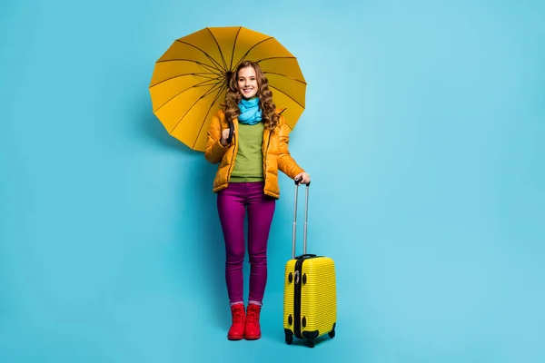 Foto de comprimento total de muito viajante senhora guarda guarda-chuva saco rolante mala de viagem do aeroporto espera usar casaco amarelo azul cachecol calças violetas botas isoladas fundo cor azul — Fotografia de Stock