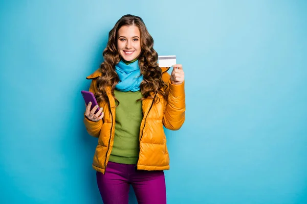 Foto de la señora bonita mantenga el teléfono haciendo la compra en línea con tarjeta de crédito de plástico pase de usar abrigo amarillo bufanda pantalones violeta jersey verde aislado color azul fondo —  Fotos de Stock