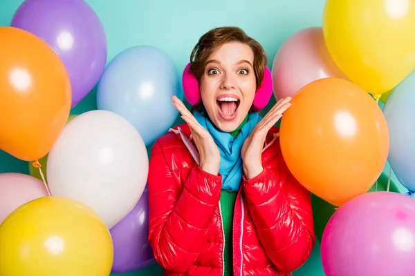 Photo of crazy lady surrounded by many colorful air balloons surprise birthday party rejoice wear casual red coat scarf jumper pink ear covers isolated teal color background