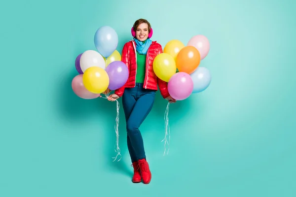 Full length photo of pretty youngster lady hold many colorful air balloons students season party wear casual red coat scarf pink ear muffs pants shoes outfit isolated teal color background