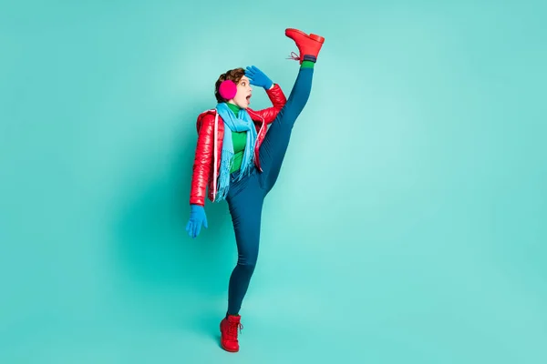 Photo du corps complet de dame drôle sans voix lever la jambe haute fraîcheur flexibilité regarder loin de la route longue porter un manteau rouge gants oreilles roses pantalons pantalons chaussures teal isolé fond de couleur — Photo