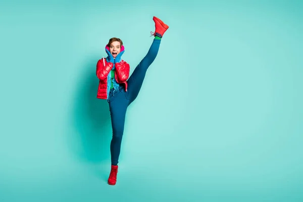 Full body photo of crazy yelling lady raise leg up high shocking flexibility after first gym training wear red overcoat gloves pink ear muffs pants shoes isolated teal color background