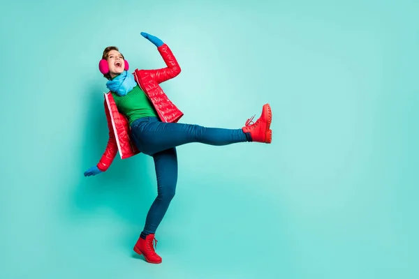 Ganzkörper-Profil-Foto von lustigen Dame tanzen auf der Straße heben Bein gute Laune tragen lässig roten Mantel Schal rosa Ohrenschützer Hose Pullover Handschuhe Schuhe isoliert teal Farbe Hintergrund — Stockfoto