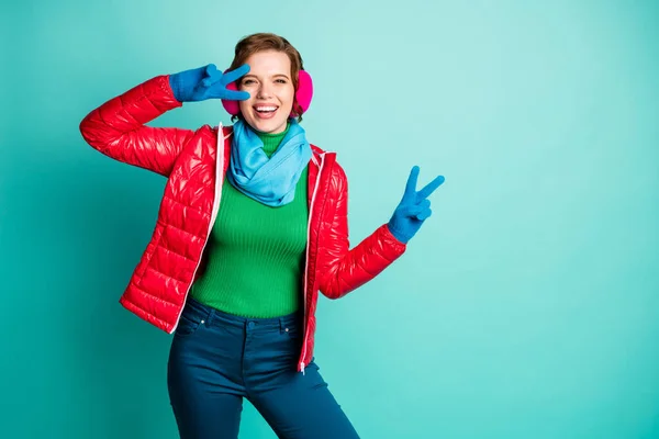 Φωτογραφία από αστείο ταξιδιώτη κυρία απολαύσετε τη χειμερινή ημέρα χαρά δείχνει σύμβολο v-σημάδι παγοδρόμιο φορούν casual κόκκινο πανωφόρι μπλε κασκόλ ροζ καλύμματα αυτιών παντελόνι απομονωμένο φόντο teal χρώμα — Φωτογραφία Αρχείου