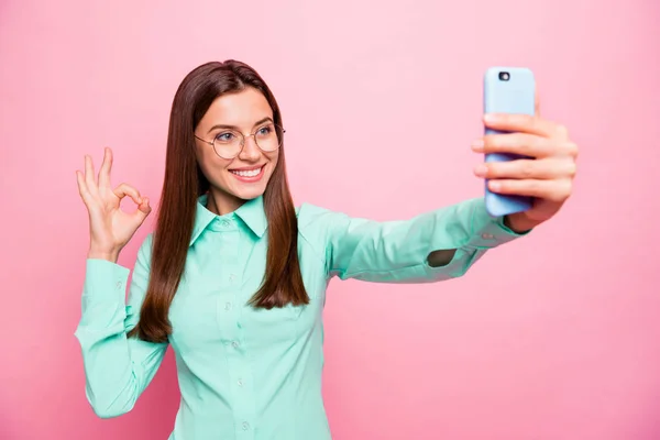 Foto de la señora bonita sosteniendo el teléfono haciendo selfies que muestran el símbolo okey de acuerdo con la calidad de la cámara increíble desgaste especificaciones camiseta verde aislado color rosa fondo —  Fotos de Stock