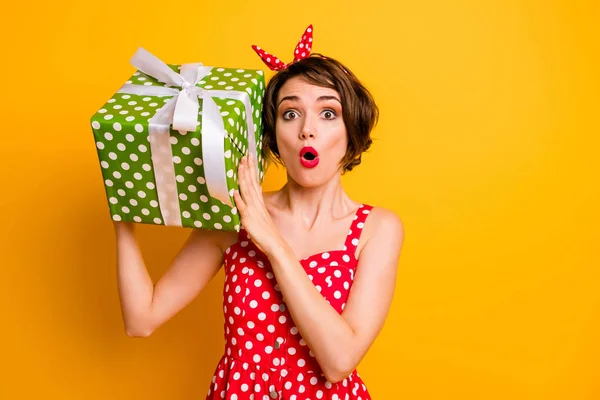 Φωτογραφία της όμορφης κυρίας κρατήσει μεγάλο πράσινο giftbox κοντά στο αυτί ανοιχτό στόμα ενθουσιασμένοι κορίτσι γενεθλίων φορούν ρετρό στυλ διάστικτη κόκκινο λευκό φόρεμα κορδέλα απομονωμένο κίτρινο χρώμα φόντο — Φωτογραφία Αρχείου
