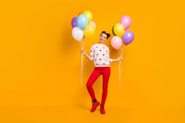 Full body photo of beautiful pretty lady bring many colorful air balloons surprise party friends event wear hearts pattern sweater red pants shoes isolated yellow color background — 스톡 사진