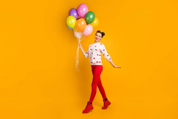 Foto de comprimento total de bela senhora transportar muitos balões de ar colorido festa surpresa andando rua desgaste corações padrão camisola calças vermelhas sapatos isolado cor amarela fundo — Fotografia de Stock