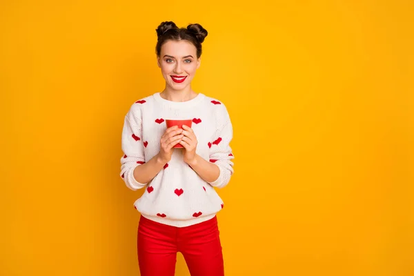 Φωτογραφία της όμορφης κυρίας κρατώντας ζεστό φλιτζάνι καφέ ρόφημα toothy χαμογελώντας απολαύσετε ελεύθερο χρόνο χαλάρωση φορούν καρδιές μοτίβο λευκό πουλόβερ κόκκινο παντελόνι απομονωμένο κίτρινο χρώμα φόντο — Φωτογραφία Αρχείου