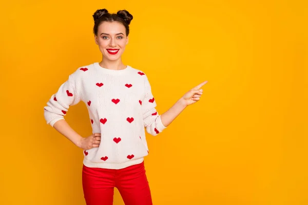 Photo of pretty funny lady showing sale low prices indicating finger empty space banner advertisement wear hearts pattern white pullover red pants isolated yellow color background — Stock Photo, Image