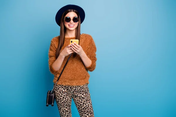 Retrato de chica alegre divertirse otoño vacaciones uso smartphone leer noticias de medios sociales desgaste gafas de sol pantalones de jersey marrón embrague retro aislado sobre fondo de color azul — Foto de Stock