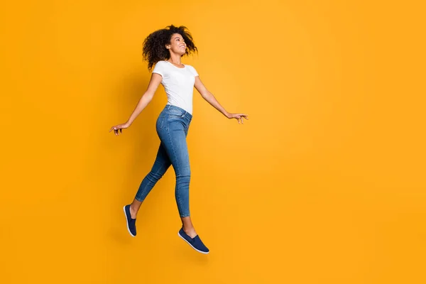 Ganzkörpergröße Seitenprofil Foto von fröhlich nett positiv erfreut Mädchen tragen Jeans Jeans weißes T-Shirt läuft Springen zu Waren diskontiert isoliert über lebendigen Farbhintergrund — Stockfoto