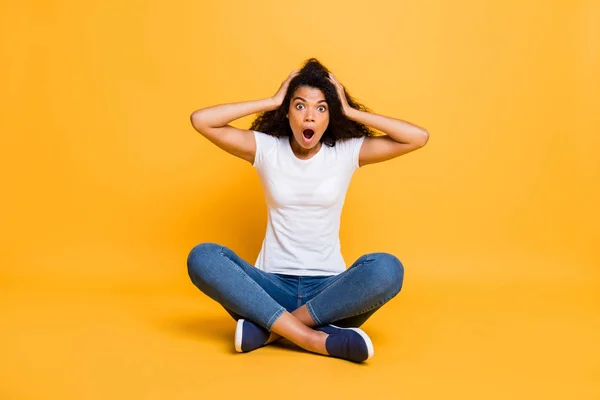 Full length body size photo of screaming shouting stunned curly wavy trendy stylish depressed youngster in jeans denim white t-shirt sitting on floor misunderstanding her failure isolated vivid yellow — Stock Photo, Image