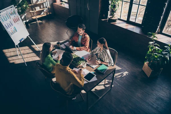 In alto sopra vista angolo alto di quattro affollati imprenditori qualificati in casual formale-wear making soluzione piano di finanziamento strategia a moderno loft industriale in legno postazione di lavoro interna — Foto Stock