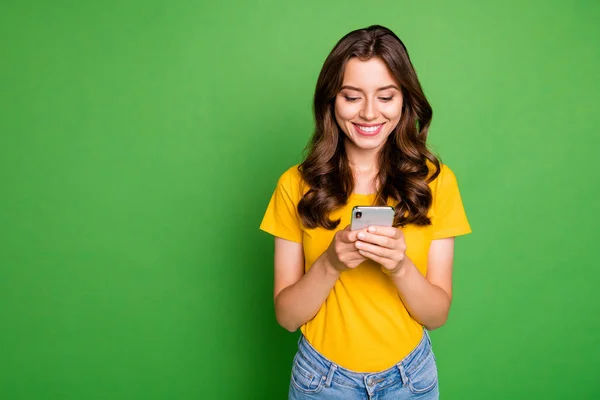 Photo of pretty wavy lady holding telephone hands reading website blog new interesting post wear casual yellow t-shirt jeans isolated bright green color background — 스톡 사진