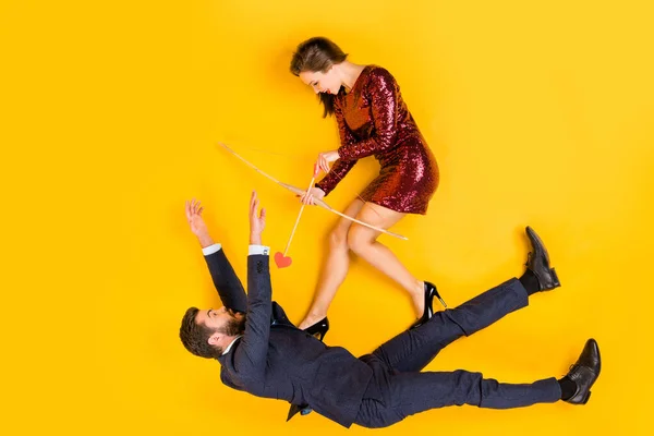 Arriba arriba de ángulo alto ver foto de cuerpo completo de dos estudiantes personas astuta chica disparar puntería flecha cupido sorprendido hombre caída desgaste rojo mini vestido esmoquin yacía aislado color amarillo fondo — Foto de Stock