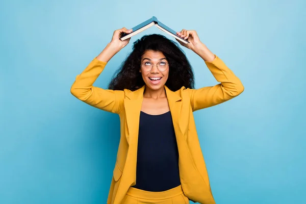 Photo of pretty dark skin wavy lady hold open book above head dont want study carefree irresponsible person wear specs stylish yellow suit blazer isolated blue color background — Stock Photo, Image