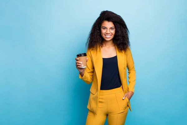 Photo of attractive chic dark skin faliste biznes lady holding hot takeout kawa napój korporacyjny obiad pauza zużycie specs żółty garnitur marynarka spodnie odizolowany niebieski kolor tło — Zdjęcie stockowe