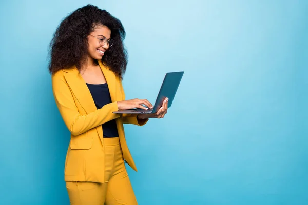 Foto de perfil de bastante asistente de piel oscura dama ondulada celebración de cuaderno de búsqueda de información de Internet ayuda jefe usar especificaciones traje amarillo pantalones de chaqueta aislado color azul de fondo —  Fotos de Stock