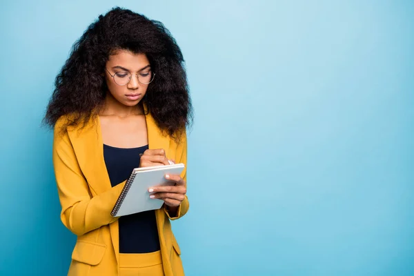 Foto von hübschen Assistenten dunkle Haut wellige Dame kreative Schreiber halten Papier Planer Stift ernst beachten Chef Wörter tragen Spezifikationen stilvolle gelbe Büro Anzug Blazer isoliert blaue Farbe Hintergrund — Stockfoto