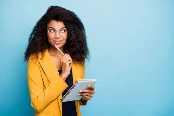 Foto de pele muito escura ondulado senhora criativo escritor segurar papel planejador caneta no queixo imaginação voo sonhador desgaste especificações elegante amarelo escritório terno blazer isolado azul cor fundo — Fotografia de Stock