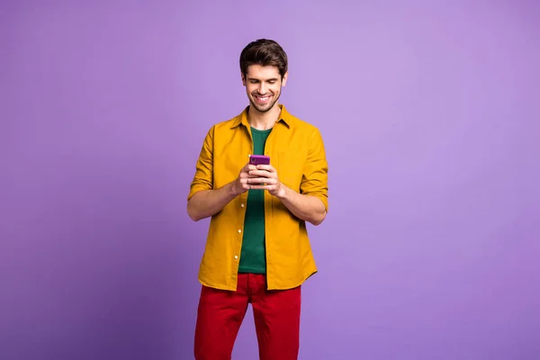 Neşeli, dişlek, ışıldayan adamın kırmızı pantolonla telefonla göz gezdirdiği fotoğraf menekşe rengi arka plan. — Stok fotoğraf
