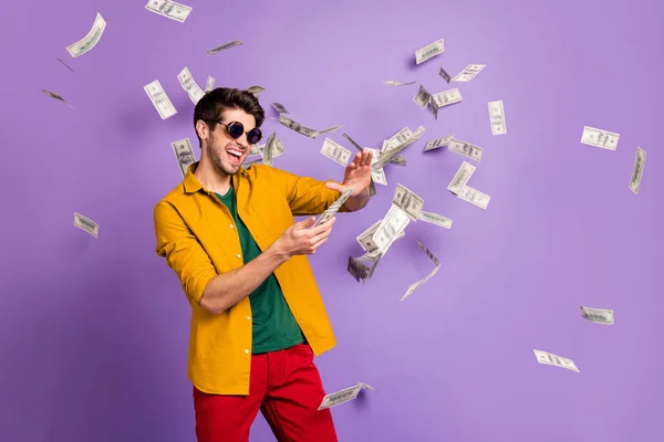 Photo of white cheerful brown haired trendy casual man with bristle throwing cash with crazy emotions on face in red pants yellow shirt isolated violet pastel color background — Stock Photo, Image